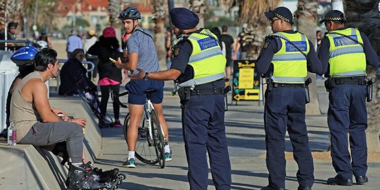 Victoria Police Protective Services Officers speak to a man at St Kilda beach in Melbourne, Monday, April 13, 2020. Victoria Police issued 433 fines between 11:00pm on Thursday and 11:00pm on Easter Sunday after conducting thousands of spot checks across the state. A shutdown of non-essential services is in effect Australia wide in a bid to slow the spread of the coronavirus (COVID-19) disease.(AAP Image/Scott Barbour) NO ARCHIVING