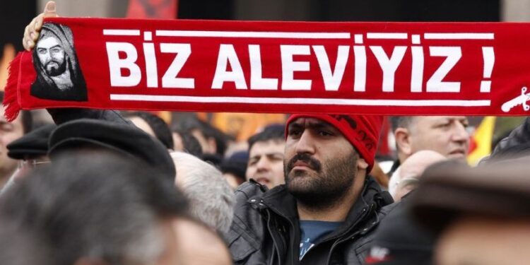 A protester holds a banner reading "we are alevi" as he and many others wait to hear the decision of the court in front of a courthouse in Ankara March 13, 2012. Turkish police fired tear-gas and water cannon to disperse hundreds protesting on Tuesday against the dropping of a case against five people charged with killing 37 writers and liberals in a 1993 hotel fire set off by Islamist rioters.The opposition accused Prime Minister Tayyip Erdogan and his AK Party, which emerged from a series of banned Islamist parties of being responsible for the failure to find the five.The case against two others charged with the kilings was dropped as the accused had died. One of them, the prime suspect who was the local mayor from the same party to which Erdogan belonged, passed away last year, close to the scene of the fire. REUTERS/Umit Bektas (TURKEY - Tags: POLITICS CIVIL UNREST)