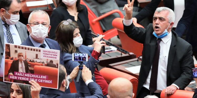 Turkish member of Parliament for the left wing political party Peoples' Democratic Party Omer Faruk Gergerlioglu (C) reacts as he is surrounded by MPs applauding and brandishing placards after he was dismissed following a vote at the Turkish Parliament in Ankara, on March 17, 2021. (Photo by Adem ALTAN / AFP)