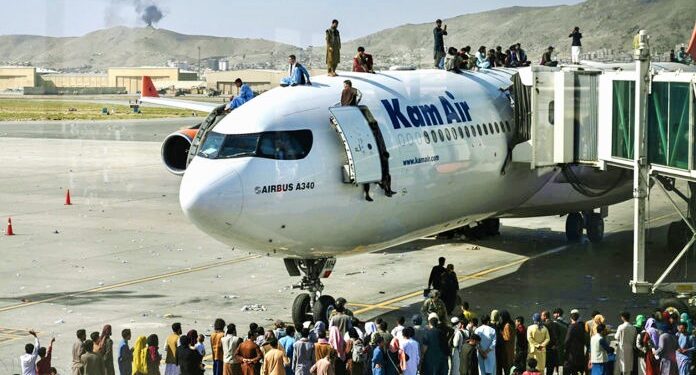 Afghan people climb atop a plane as they wait at the Kabul airport in Kabul on August 16, 2021, after a stunningly swift end to Afghanistan's 20-year war, as thousands of people mobbed the city's airport trying to flee the group's feared hardline brand of Islamist rule. (Photo by Wakil Kohsar / AFP)