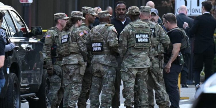 National Guard soldiers huddle around law enforcement officers while receiving information after a shooting in downtown Washington, DC, on November 26, 2025. Two National Guard soldiers were shot a few blocks from the White House, according to law enforcement. (Photo by Drew ANGERER / AFP)